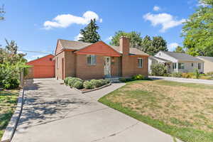 View of front of home with a chimney, brick siding, a front yard, a garage, and an outbuilding