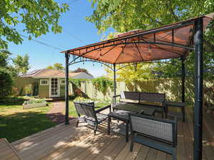 Wooden terrace featuring an outdoor hangout area, a fenced backyard, a gazebo, and an outbuilding