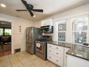 Kitchen with stainless steel appliances, dark stone counters, white cabinetry, light tile patterned flooring, and ceiling fan