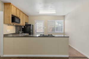 Kitchen featuring a peninsula, backsplash, black appliances, dark stone countertops, and light tile patterned flooring