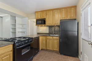 Kitchen featuring black appliances, light tile patterned flooring, dark stone counters, and tasteful backsplash