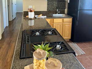 Kitchen with black appliances, decorative backsplash, dark stone countertops, and light brown cabinetry