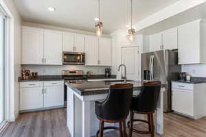 Kitchen with stainless steel appliances, decorative light fixtures, light wood finished floors, a center island with sink, and recessed lighting