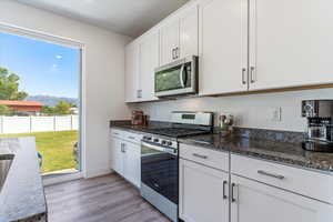 Kitchen featuring appliances with stainless steel finishes, white cabinetry, light wood finished floors, dark stone countertops, and a mountain view