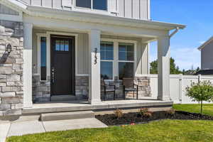 Doorway to property with board and batten siding, stone siding, and a porch
