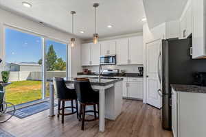 Kitchen featuring light wood-style floors, white cabinets, hanging light fixtures, an island with sink, and recessed lighting