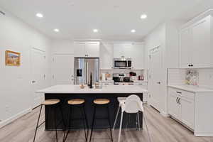 Kitchen featuring a kitchen island with sink, a breakfast bar, decorative backsplash, stainless steel appliances, and recessed lighting
