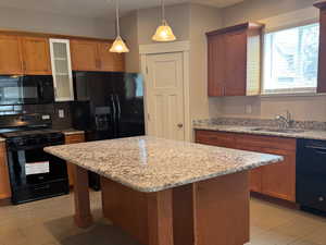 Kitchen with black appliances, light stone counters, recessed lighting, backsplash, and a kitchen bar