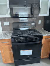 Kitchen featuring black appliances, decorative backsplash, light stone countertops, and beautiful cabinets