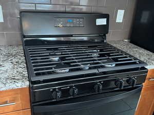 Kitchen view of brand new black gas stove, light stone countertops,  tasteful backsplash, with spacious pantry.