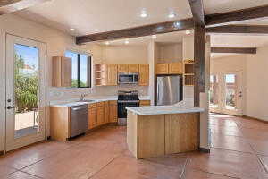 Kitchen featuring open shelves, beam ceiling, stainless steel appliances, light countertops, and a peninsula