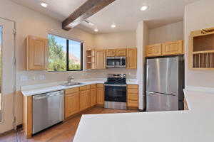 Kitchen with light countertops, appliances with stainless steel finishes, open shelves, beam ceiling, and recessed lighting