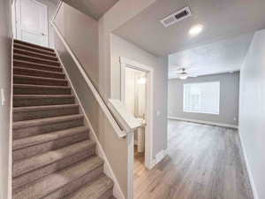 Staircase with a textured ceiling, wood finished floors, and a ceiling fan