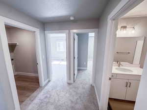 Hall with a textured ceiling, light colored carpet, and light wood-type flooring