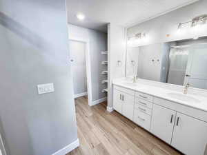 Bathroom with a textured ceiling, light wood-type flooring, double vanity, a stall shower, and a closet