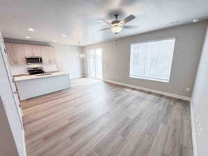Kitchen with light countertops, open floor plan, a textured ceiling, appliances with stainless steel finishes, and hanging light fixtures