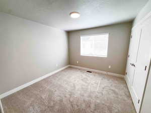Unfurnished bedroom with a textured ceiling, a closet, and light colored carpet