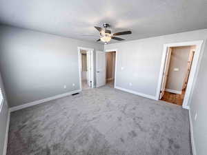 Unfurnished bedroom with carpet flooring, a walk in closet, a textured ceiling, and a ceiling fan