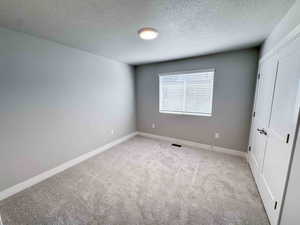 Unfurnished bedroom with light carpet, a textured ceiling, and a closet