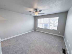 Empty room featuring a textured ceiling, carpet floors, and ceiling fan