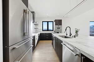Kitchen with appliances with stainless steel finishes, light stone countertops, modern cabinets, wall chimney exhaust hood, and backsplash