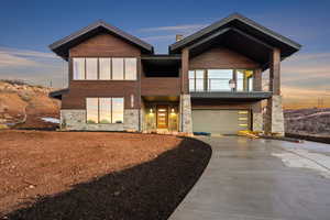 Contemporary house with concrete driveway, stone siding, a balcony, and a garage