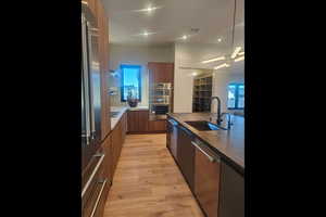 Kitchen featuring modern cabinets, light wood finished floors, stainless steel appliances, brown cabinetry, and dark stone countertops