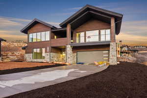 Modern home with concrete driveway, stone siding, a balcony, and a garage