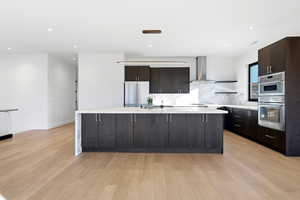 Kitchen with modern cabinets, an island with sink, dark brown cabinetry, backsplash, and light wood-style flooring