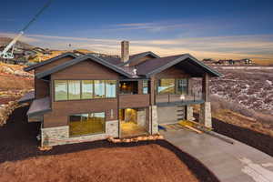 View of front of home featuring stone siding, a balcony, driveway, and an attached garage