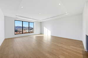 Unfurnished room with light wood finished floors, a mountain view, a tray ceiling, and recessed lighting