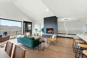 Living area featuring a mountain view, light wood-style flooring, a tiled fireplace, vaulted ceiling, and recessed lighting