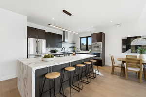 Kitchen with light stone countertops, a breakfast bar area, stainless steel refrigerator, dark wood finish cabinets, and light wood-style flooring
