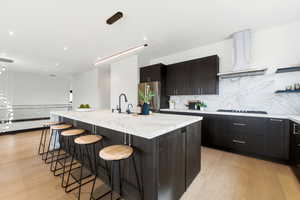 Kitchen featuring a breakfast bar, an island with sink, dark wood finish cabinets, light wood-type flooring, and modern cabinets