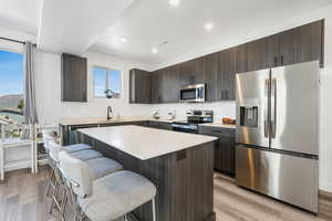 Kitchen featuring stainless steel appliances, dark brown cabinets, a center island, light wood finished floors, and a breakfast bar