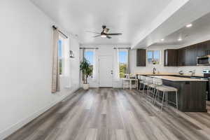 Kitchen with a breakfast bar, dark brown cabinets, appliances with stainless steel finishes, light countertops, and light wood finished floors