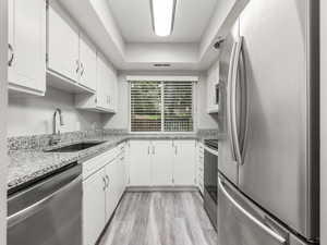 Kitchen with stainless steel appliances, light stone countertops, white cabinets, and light wood-type flooring