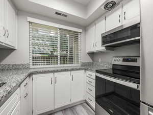Kitchen featuring appliances with stainless steel finishes, white cabinets, light stone countertops, and light wood-type flooring