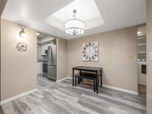 Dining room featuring a raised ceiling, washer / dryer, light wood-type flooring, and a chandelier