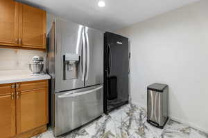 Kitchen with stainless steel fridge, tan cabinetry, light countertops, light marble finish floors, and recessed lighting