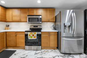 Kitchen with stainless steel appliances, light countertops, light marble finish floors, tan cabinetry, and recessed lighting