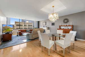 Dining room with a raised ceiling, light hard wood laminate floors, and a chandelier
