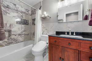Full bath with marbe shower / cast iron bath combination with curtain, granite vanity, and marble tile walls