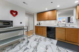 Kitchen featuring light countertops, black dishwasher, tan cabinetry, recessed lighting, and light marble finish flooring