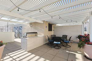View of roof top patio with area for grilling, outdoor dining area, and a pergola with spritzers