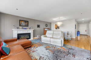 Living room with light hard wood laminate floors, a glass covered electric fireplace, and a chandelier