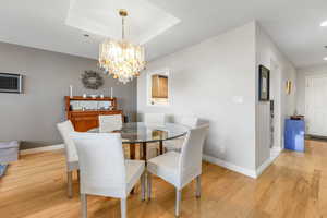 Dining area featuring a raised ceiling, light hard wood laminate floors, a chandelier, and recessed lighting