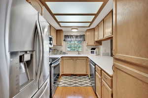 Kitchen with stainless steel appliances, light brown cabinets, light countertops, and light wood-style floors