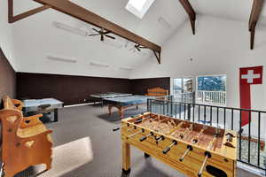 Recreation room with high vaulted ceiling, a skylight, carpet floors, beamed ceiling, and ceiling fan