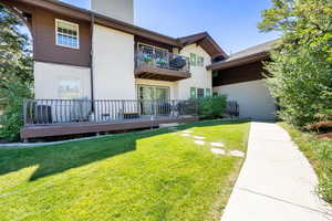 Back of property with a balcony, a yard, stucco siding, and a deck